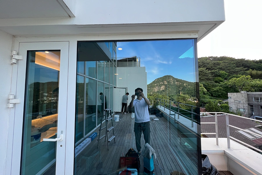 발코니 통유리에 필름 작업 중인 시공팀 모습과 산 전망