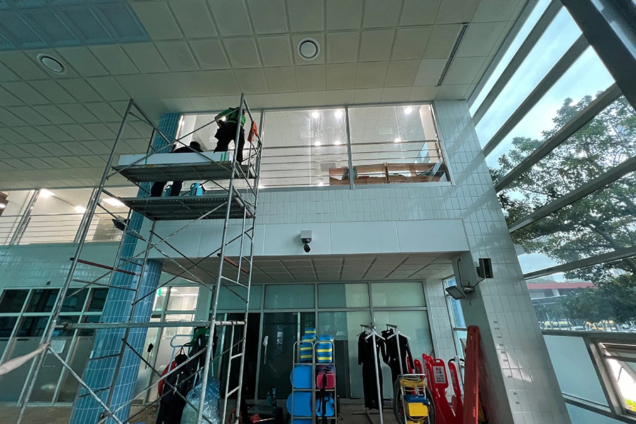 수영장 위에 설치된 알루미늄 스캐폴딩 작업대와 고측창 필름 시공 중인 두 명의 작업자